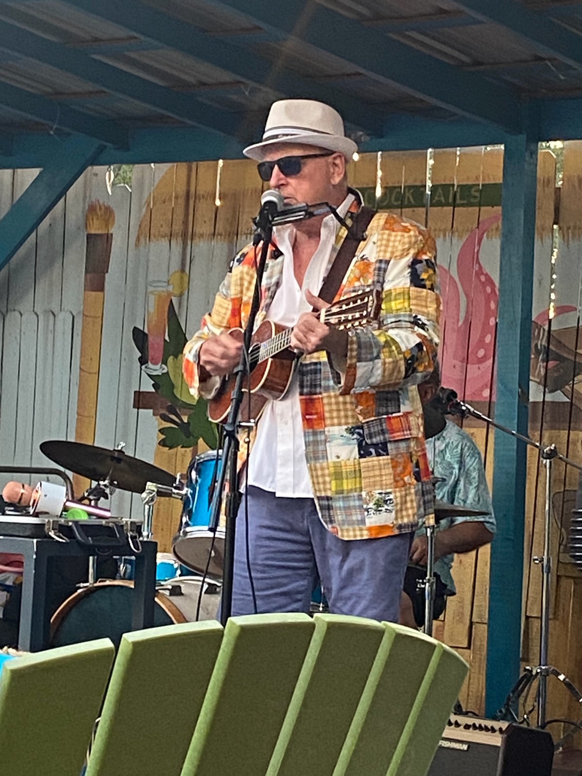 Tom Hood in a patchwork jacket playing ukulele on an outdoor tiki-bar stage